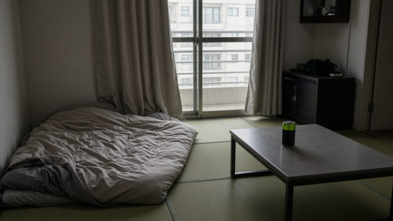 カーテンを半分閉めた午後の部屋と、また使われている布団